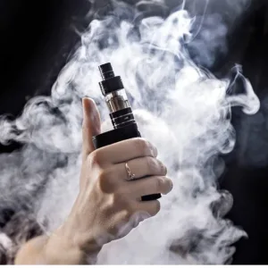 A hand holding a black vape device surrounded by thick vapor clouds against a dark background.